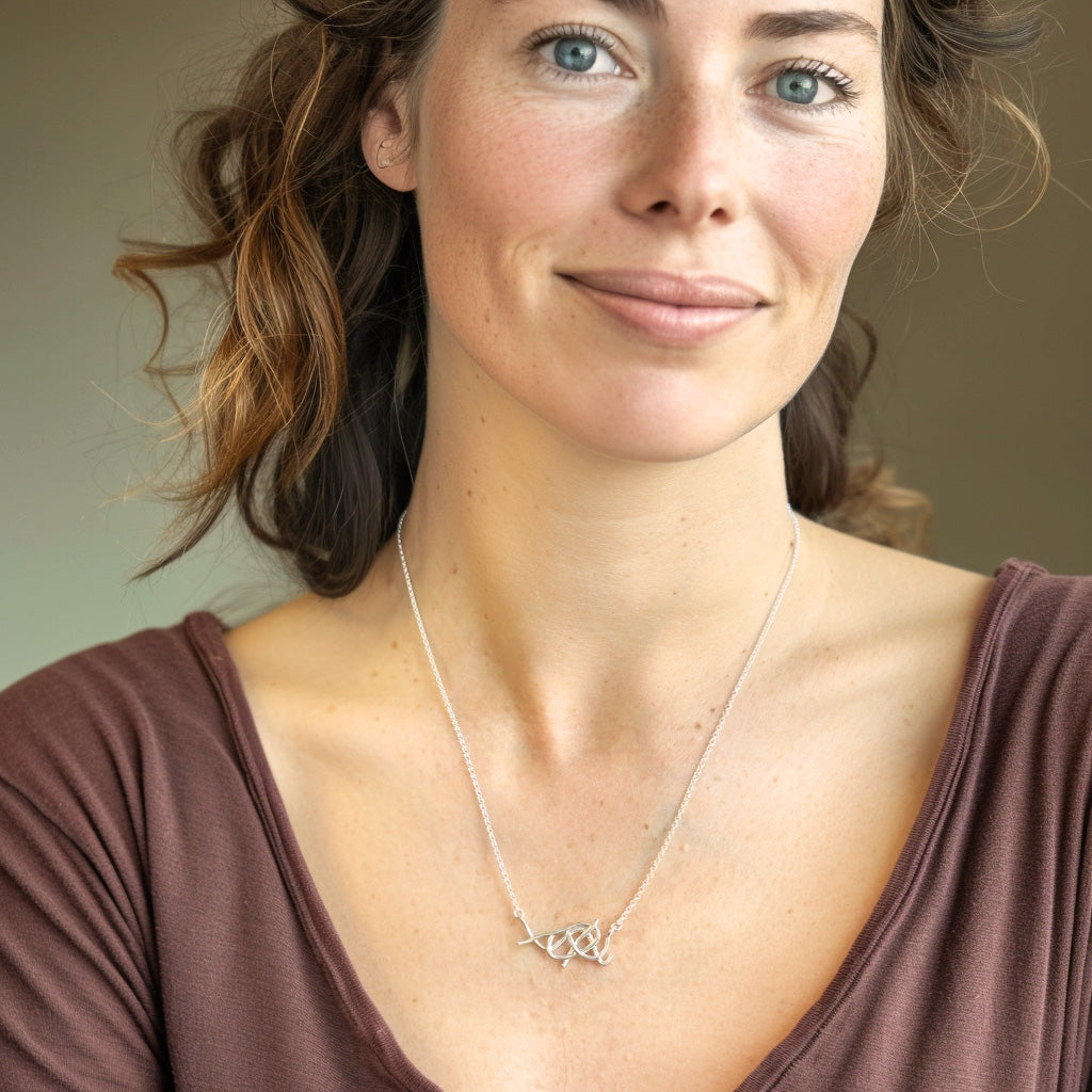 Smiling woman wearing a nanofibers necklace in sterling silver, paired with a V-neck brown top, showcasing the jewelry as a subtle scientific statement piece.