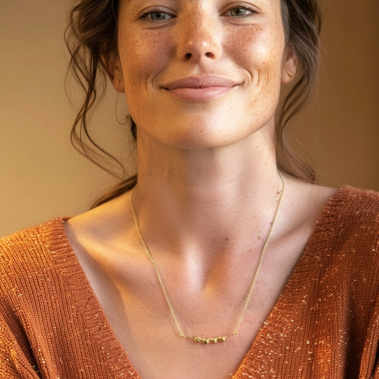 Smiling woman wearing a gold vermeil nucleosome necklace layered with a second chain, styled with a soft brown top.