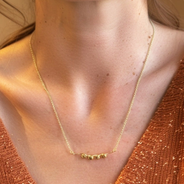 Close-up of a woman’s neck showing the gold vermeil nucleosome necklace resting just below the collarbone.