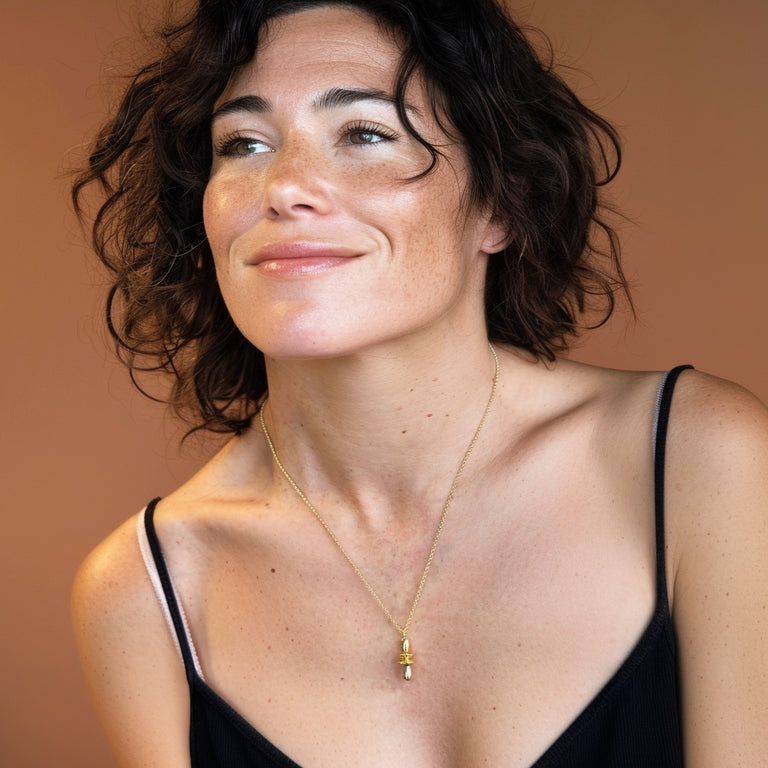 Smiling woman wearing the gold vermeil orbital necklace against a warm background, highlighting the pendant’s golden shine and modern scientific design.