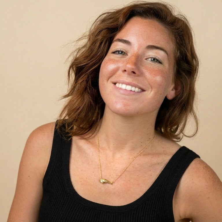 Smiling woman wearing a black tank top and the gold vermeil pancreas necklace. The pendant rests at the center of her chest.