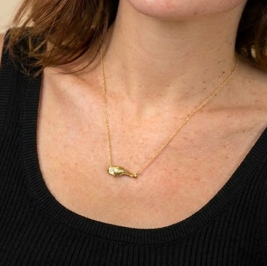 Close-up of the gold vermeil pancreas necklace worn around the neck. The anatomical pendant hangs centrally against the skin, with a black top visible.