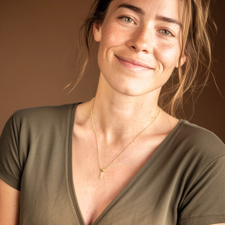 Smiling woman wearing the Phospholipid Necklace in gold vermeil, styled with a v-neck top, showing the jewelry’s simple and modern look.