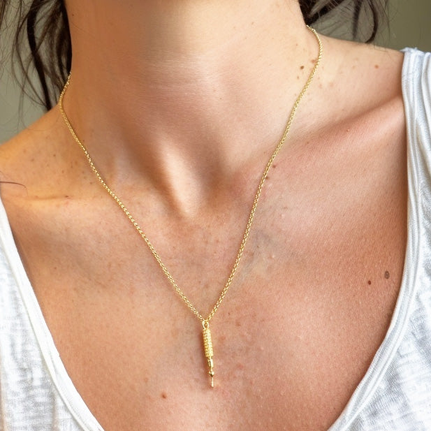 Gold vermeil photoreceptor necklace worn on a model with a white top, shown as a delicate pendant resting on the chest.