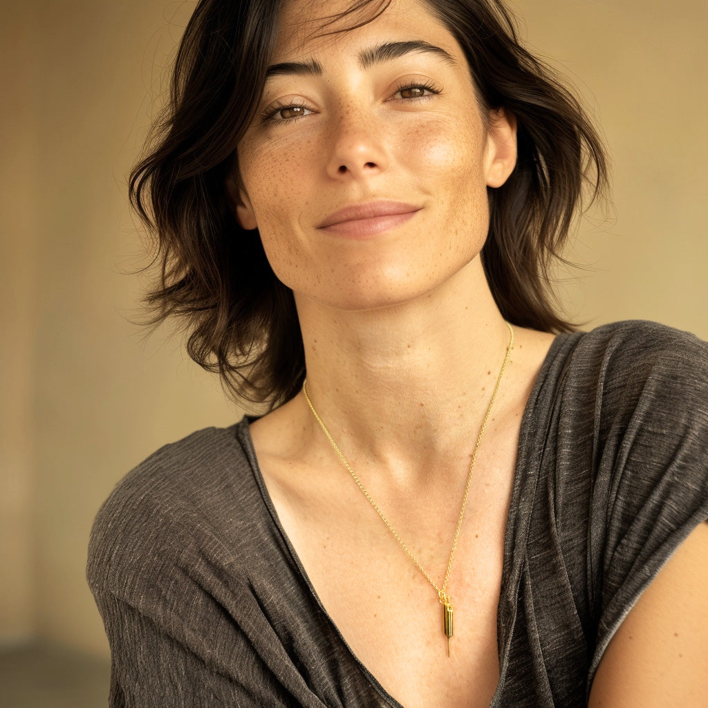 Smiling woman with short dark hair wearing the gold vermeil pipette necklace on a fine chain, styled with a casual grey top.