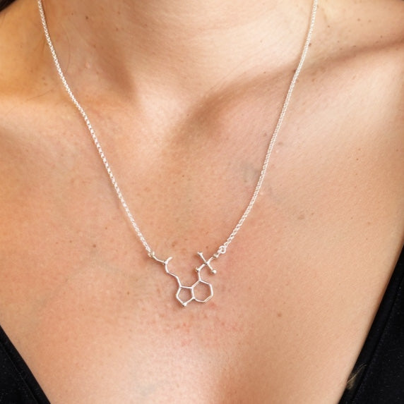 Close-up of psilocybin molecule necklace resting on the collarbone, detailed sterling silver science jewelry symbolizing psychedelic chemistry and discovery.