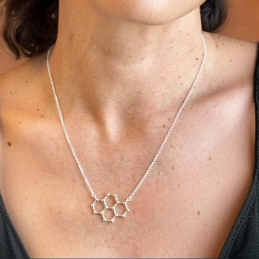 Close-up of the silver pyrene necklace worn around the neck, showing the minimalist molecular pendant resting on skin — elegant science jewelry design inspired by chemistry.