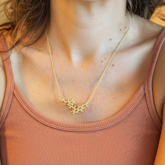 A woman wearing a simple tank top showcases a vermeil gold quinine molecule necklace resting just below her collarbones.