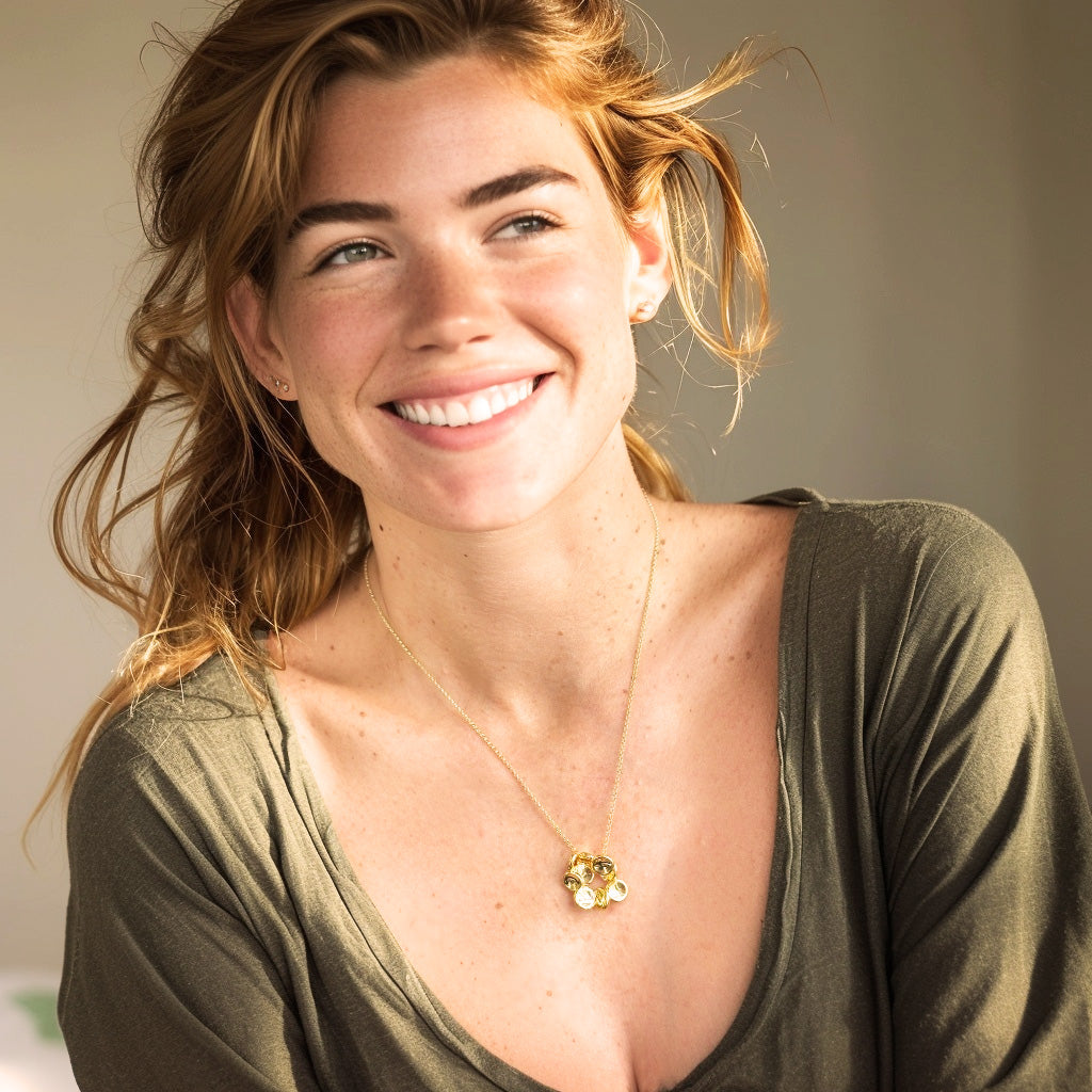 Smiling woman with light brown hair wearing a green top and a gold vermeil red blood cell necklace.