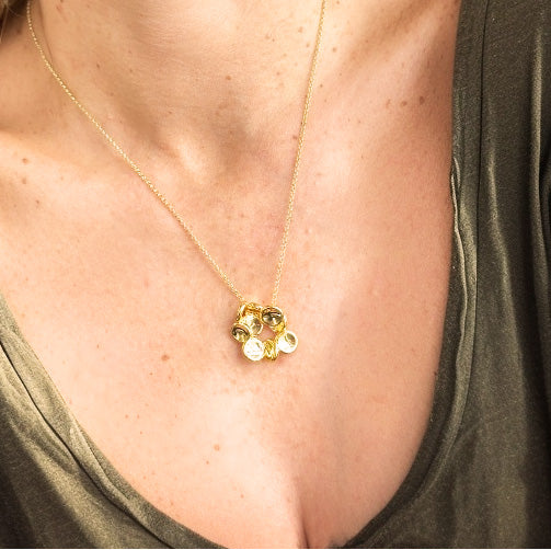 Gold vermeil red blood cell necklace hanging on a fine chain, shown against a woman’s skin and green top