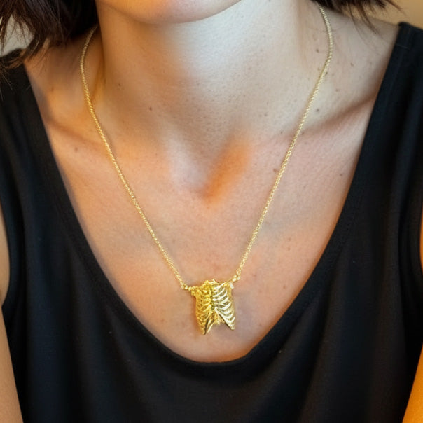 Close-up of a gold vermeil rib cage pendant necklace worn over a black top, highlighting the anatomical thorax design.