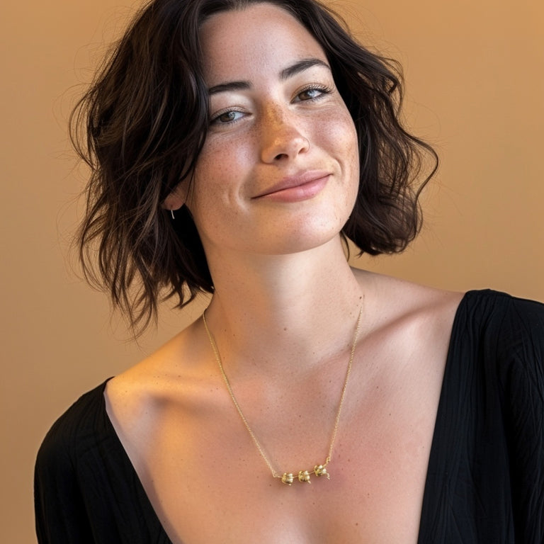 Portrait of a woman wearing the gold vermeil ribosome necklace, showing how the ribosomal pendant sits at mid-chest length against a warm background.