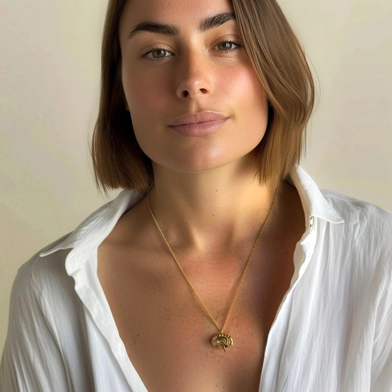 Portrait of a woman wearing the gold sagittal brain necklace, smiling subtly in a white blouse with the pendant prominently displayed.