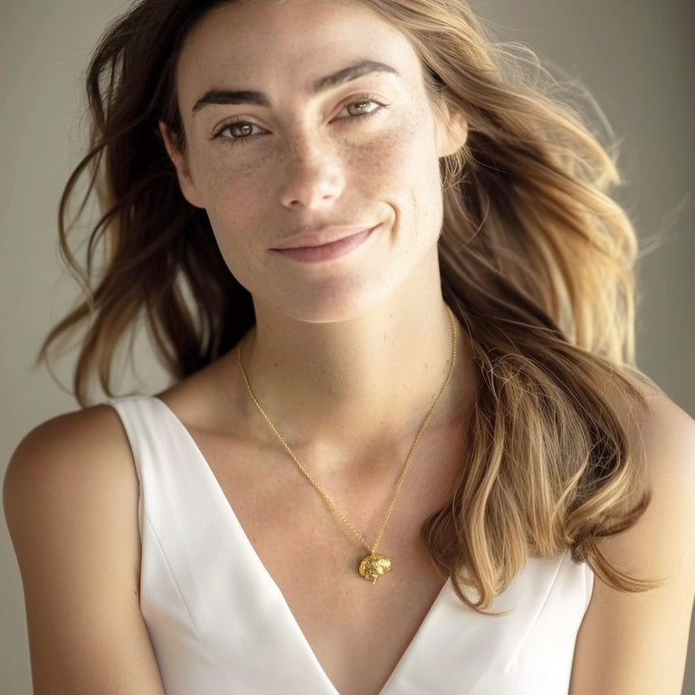 Smiling woman with long wavy hair wearing a gold vermeil sagittal brain necklace against a sleeveless white top.