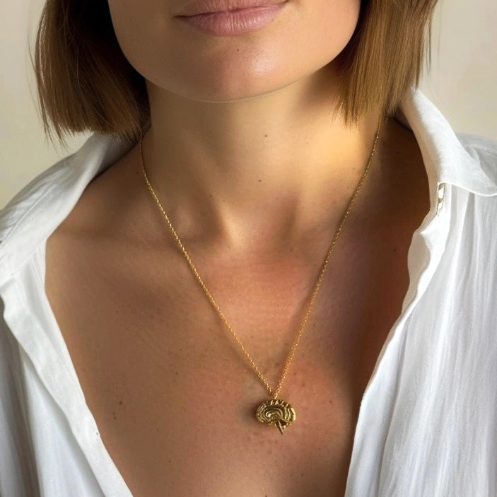 Close-up of a woman wearing the gold sagittal brain necklace over a white shirt, highlighting the pendant’s position and size.