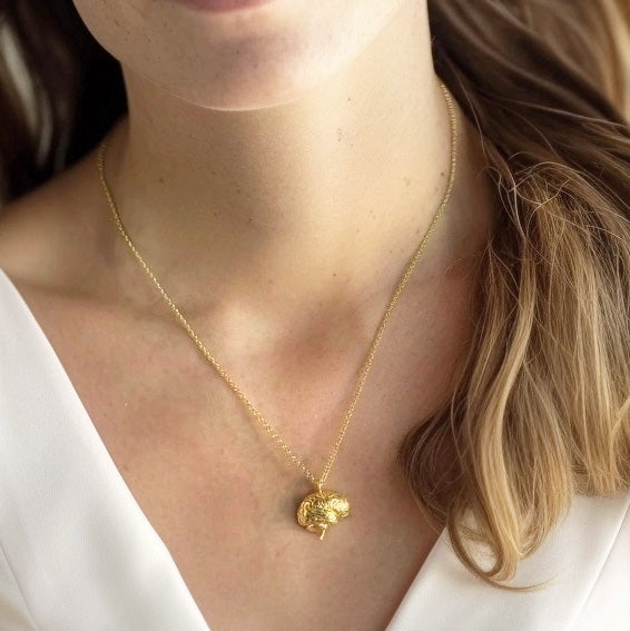 Close-up of a gold vermeil sagittal brain necklace worn over a white top, showcasing the detailed anatomical pendant.