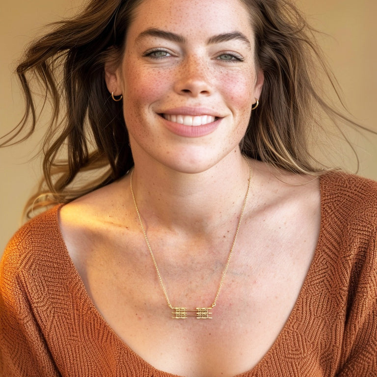 Smiling woman wearing the gold vermeil sarcomere necklace, with the pendant clearly visible against a soft brown sweater, showing size and how the piece sits when worn.