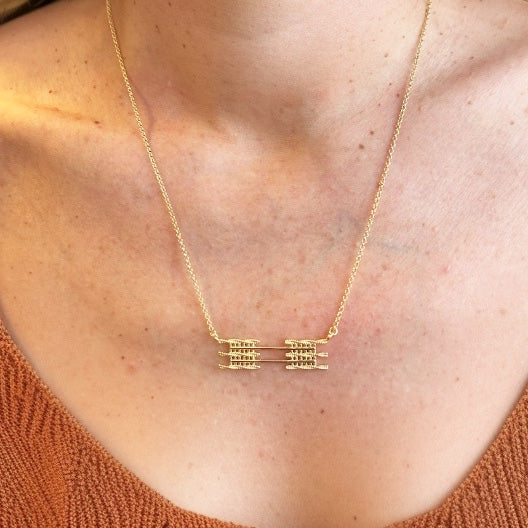 Close-up of the gold vermeil sarcomere necklace worn around the neck, showing the detailed banded muscle-fiber pendant resting just below the collarbone.