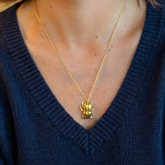 Close up of a person wearing the gold vermeil scarab beetle necklace over a dark blue V-neck sweater.