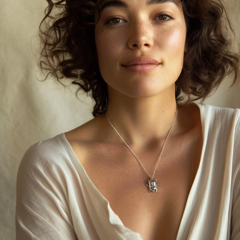 Woman wearing the scarab beetle necklace on a fine silver chain, styled with a cream-colored blouse, softly lit in a natural setting.