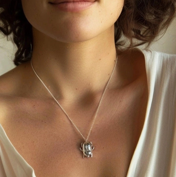 Close-up of scarab beetle necklace worn around the neck, emphasizing the pendant’s intricate beetle design against bare skin and light fabric.