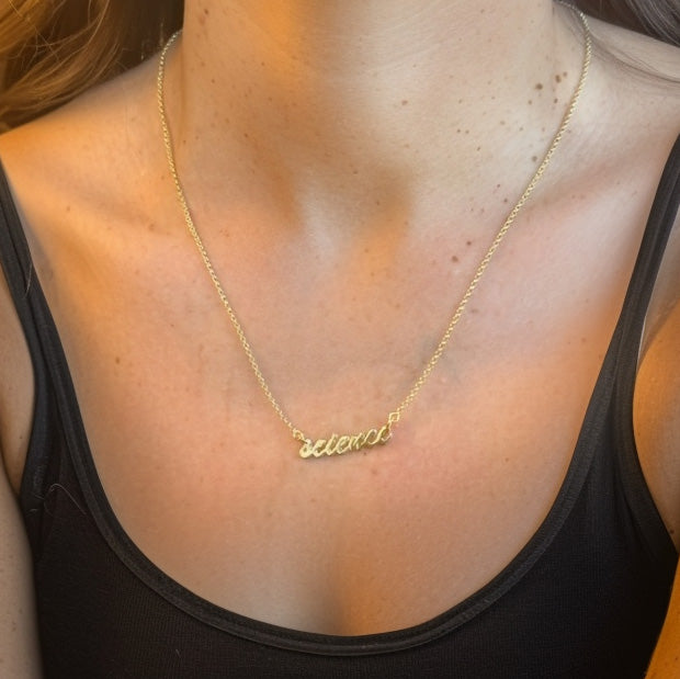 Close-up view of a woman wearing the gold vermeil ‘science’ necklace, shown against a black top with focus on her collarbones and the pendant.