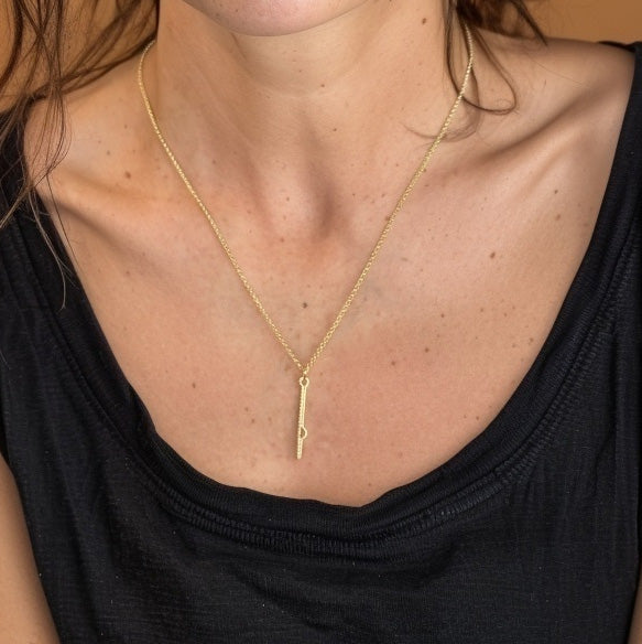 Woman wearing the vertical shRNA gold vermeil necklace with a low-cut black top, showing how the pendant hangs gracefully along the neckline.
