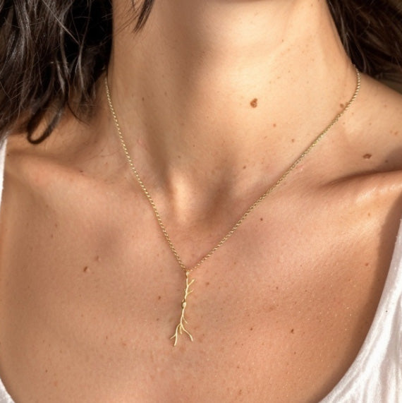 Close-up view of a woman wearing the gold vermeil spindle neuron necklace, showing the pendant resting on her chest for scale and detail.