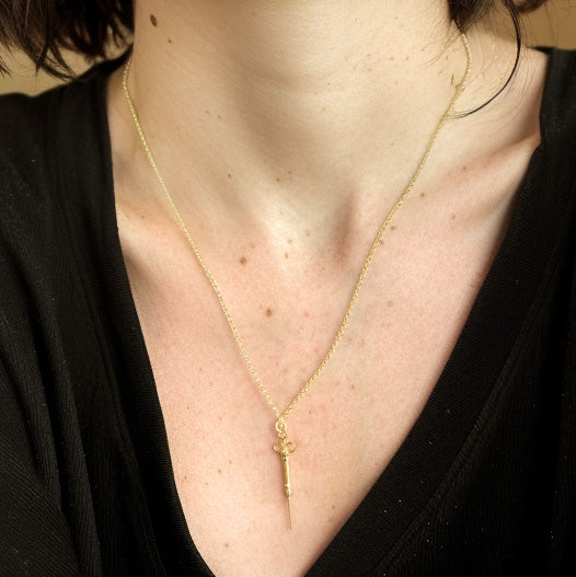 Close-up of a gold vermeil syringe necklace hanging on a woman’s chest, paired with a simple chain.