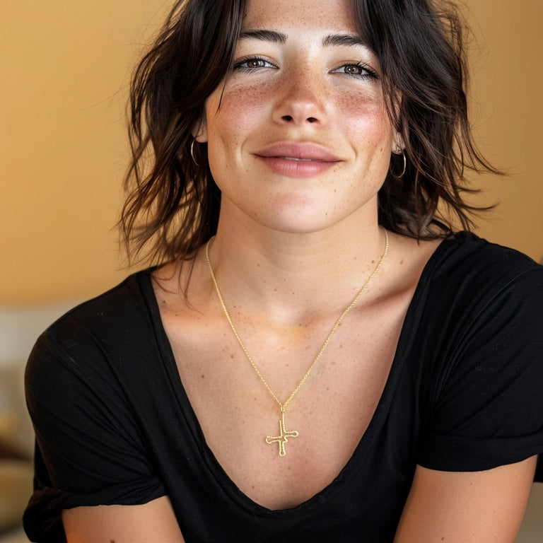 Smiling woman wearing the gold vermeil tRNA necklace with a black shirt, highlighting the modern, science-inspired cloverleaf pendant design.