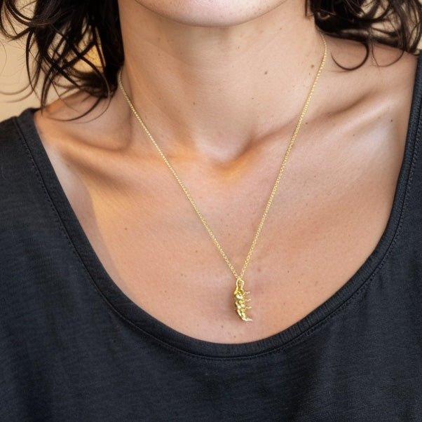 Woman wearing the gold vermeil tardigrade necklace, pendant resting at mid-chest level, highlighting its size and shine against a dark shirt.