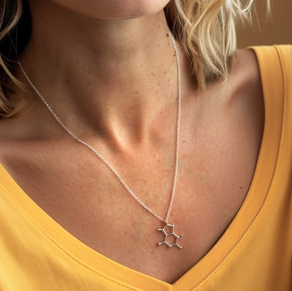 Close-up of a silver theobromine molecule necklace worn by a woman in a yellow top.