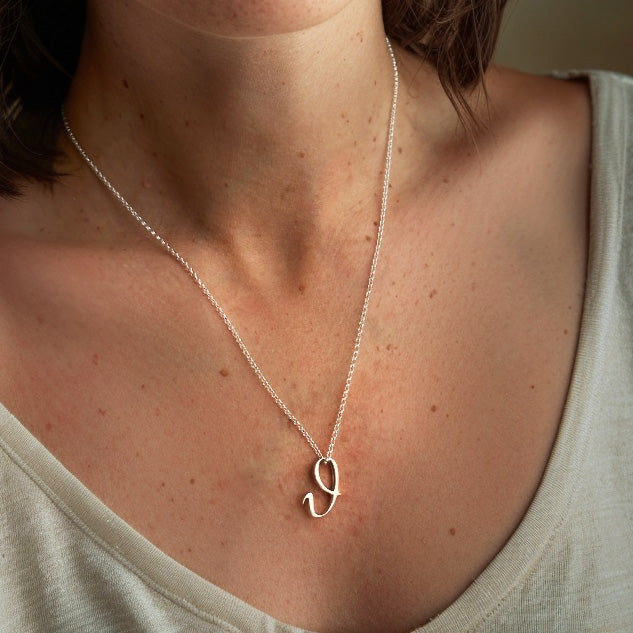 Close-up of a sterling silver theta necklace resting on a woman’s collarbone, worn over a light-colored shirt.