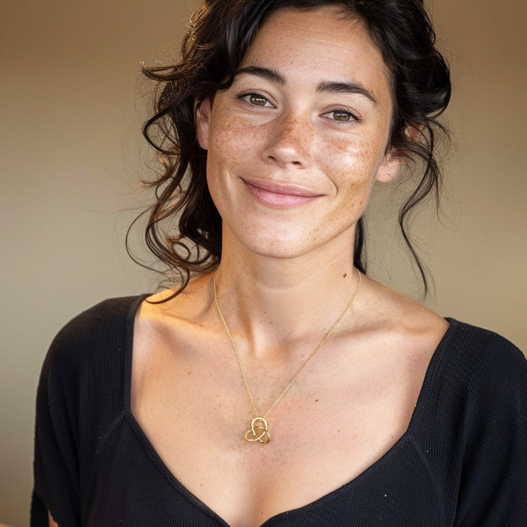 Woman wearing the Trefoil Knot Necklace in gold vermeil, smiling and dressed in a black top — showing the pendant’s elegant size and warm golden shine against the skin.