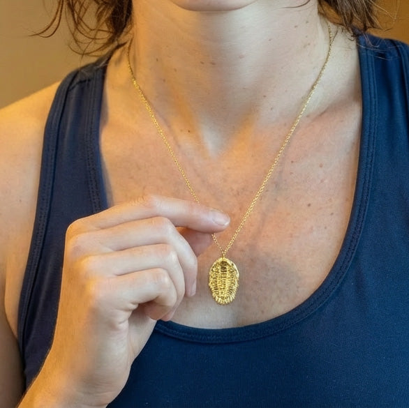 Person wearing a gold vermeil trilobite necklace, holding the pendant at chest height to show scale and detail.