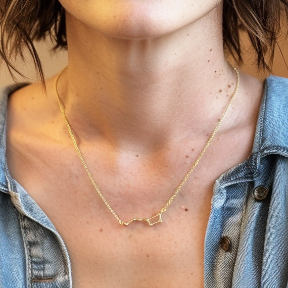 Close-up of a person wearing the gold vermeil Ursa Major constellation necklace, layered with a second chain and styled with a denim shirt.