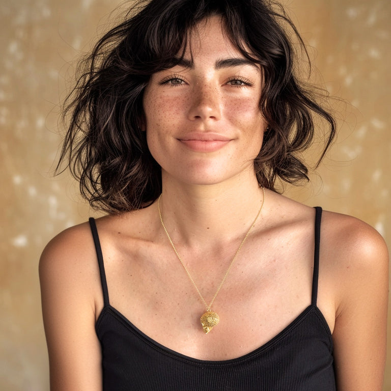 Smiling woman with short dark hair wearing the gold vermeil Voronoi Skull Necklace over a black top, shown from the shoulders up.