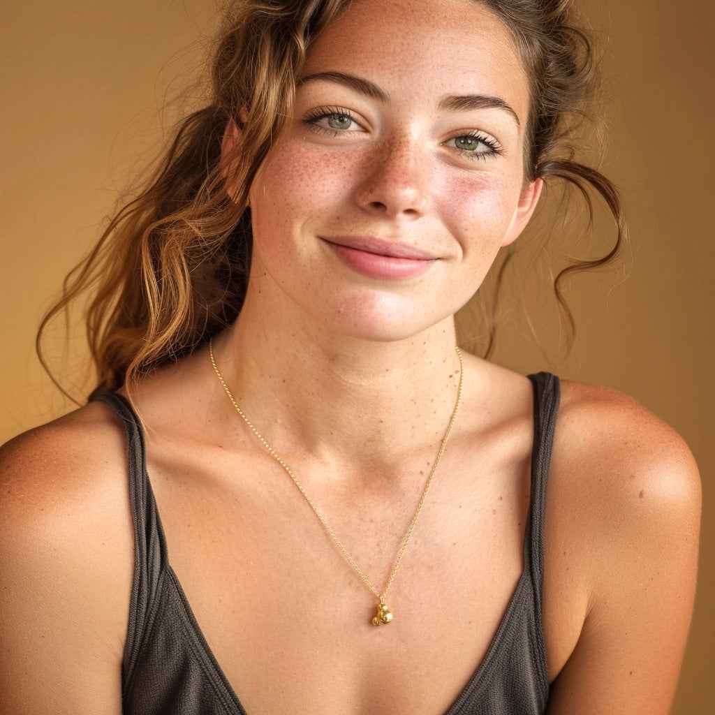 Smiling woman wearing a gold vermeil H2O necklace, with the pendant resting on her chest, styled in a casual outfit.