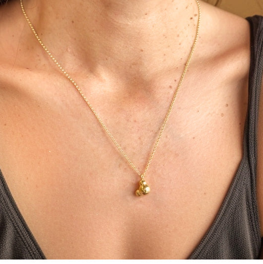 Close-up of a gold vermeil H2O necklace pendant resting on a woman’s chest, highlighting the delicate chain and molecular design.