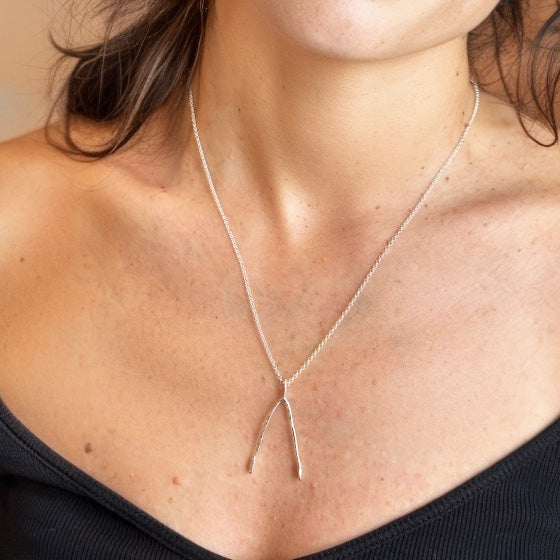 Close-up of silver wishbone pendant on model’s neck — anatomical jewelry symbolizing resilience, luck, and the beauty of scientific design.